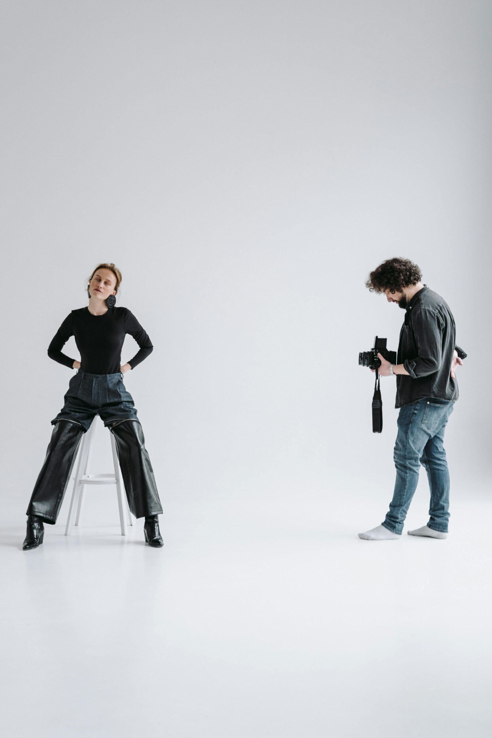 A professional photographer capturing a seated model during a studio photoshoot with a white background.